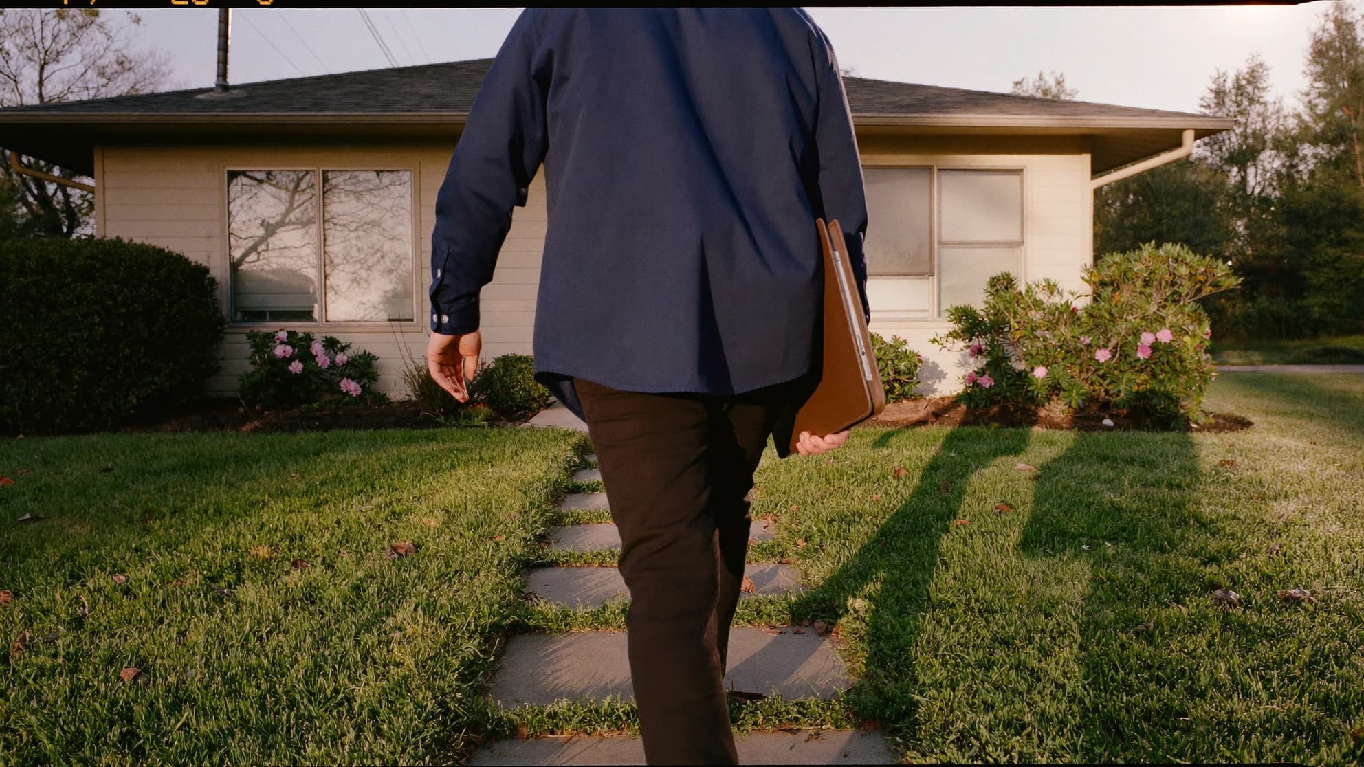 An agent walking up the front walk of a modest single-story home in early morning light